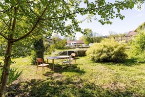 Ein Garten mit Tisch und Stühlen, umgeben von Pflanzen und einem Baum.