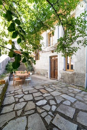 Ein mit Steinplatten gepflasterter Innenhof mit Außenbestuhlung, einer Treppe und einem Gebäude mit einer Holztür.