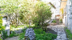 Un sendero de piedra que lleva a una escalera de madera, rodeado de vegetación y un muro de piedra.