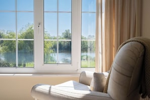 Ein Zimmer mit Blick auf einen See, mit einer großen Fensterfront, einem Sofa und einem Vorhang.