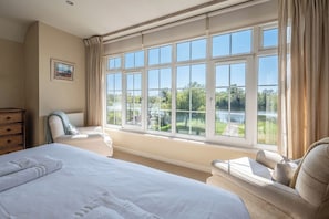 Ein Schlafzimmer mit großem Fenster, einem Bett, einem Sessel und einer Kommode.