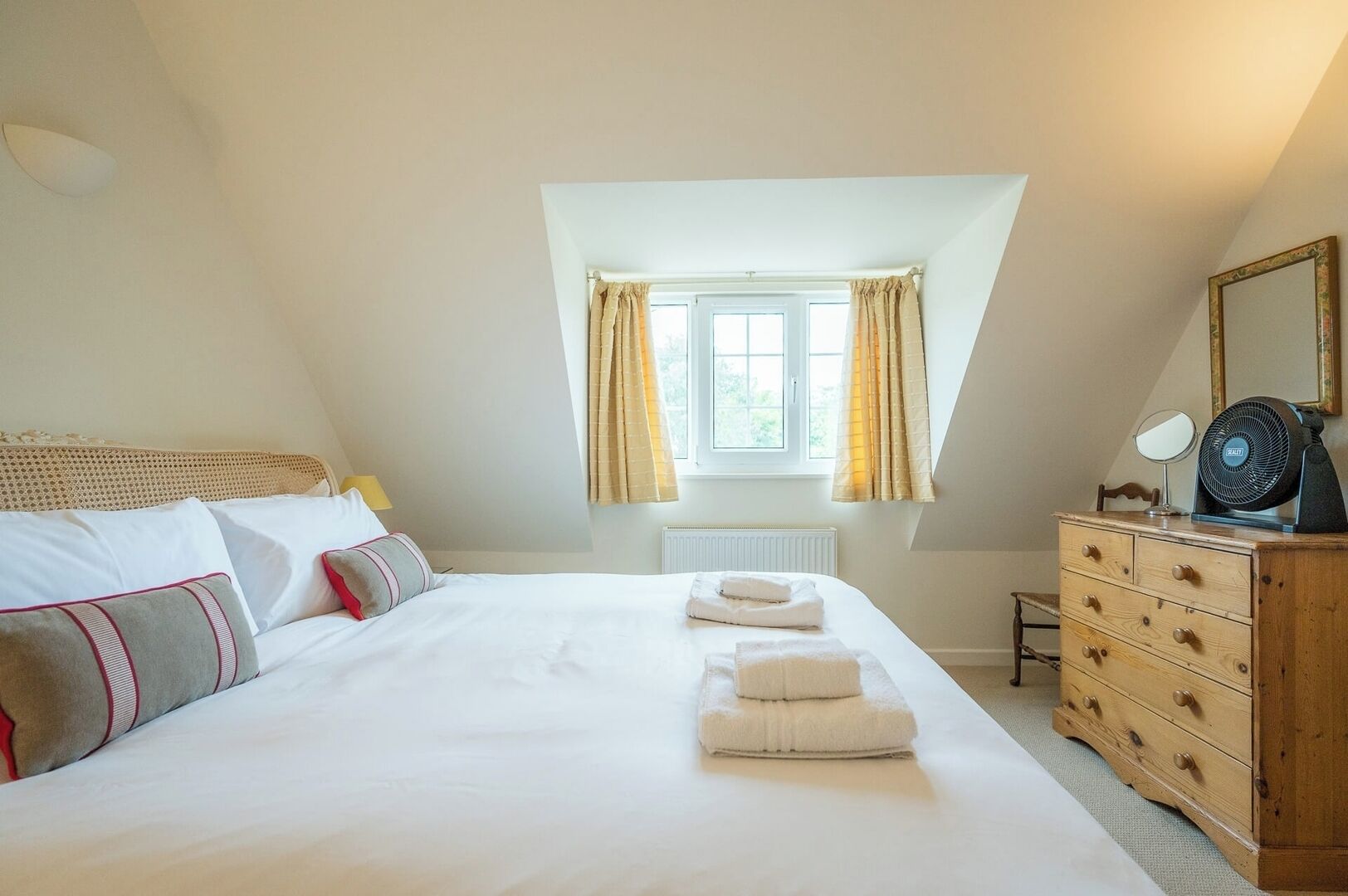 Une chambre à coucher avec un grand lit, une commode, un miroir et une fenêtre avec des rideaux.