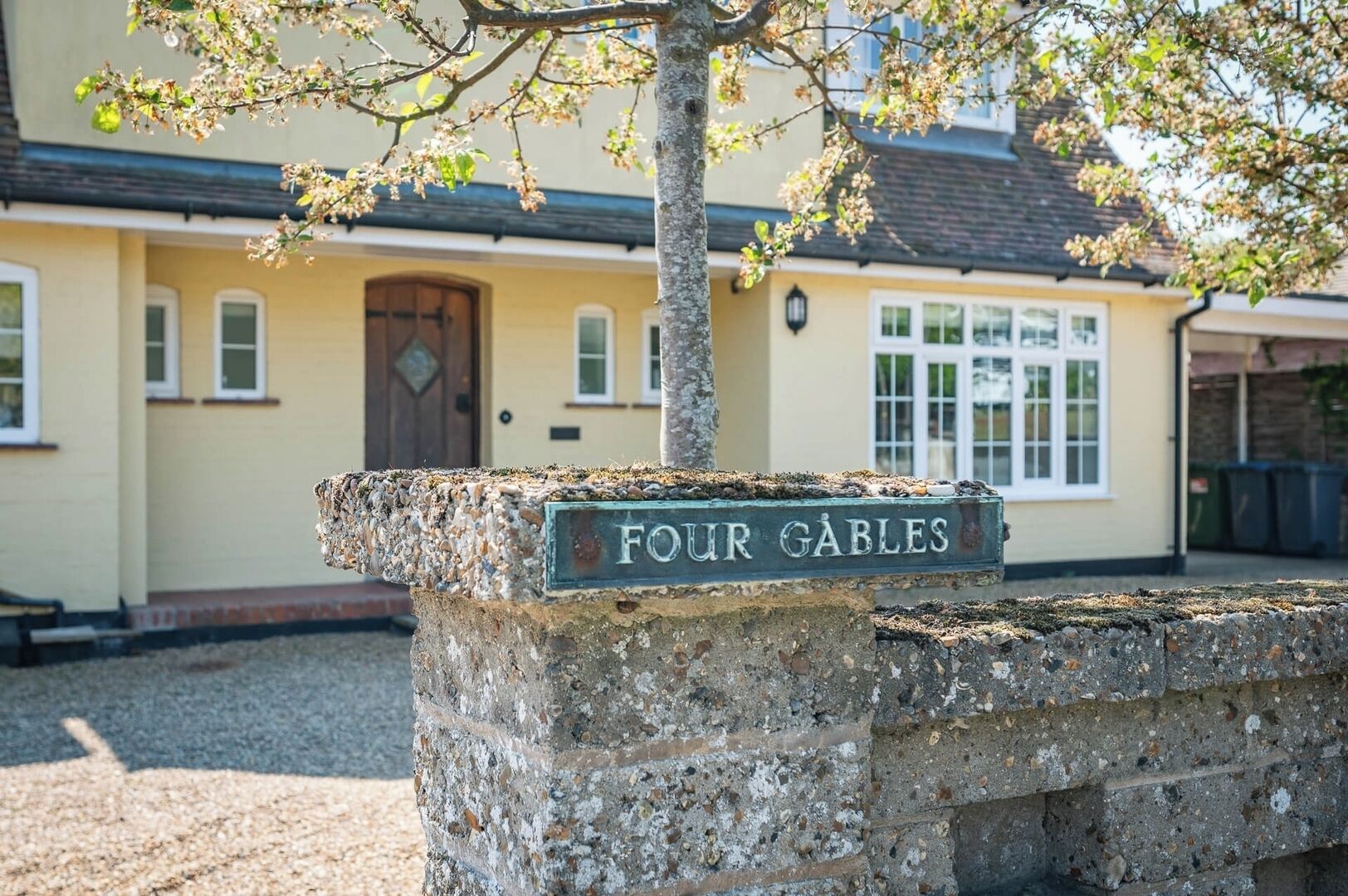 A stone wall with a sign reading 'FOUR GABLES' in front of a building with a yellow facade and a brown door.