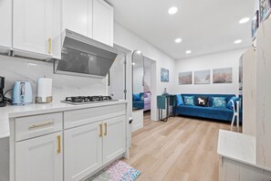 Une cuisine moderne avec des armoires blanches, une cuisinière à gaz et un four encastré. Le salon est aménagé avec un canapé bleu et une petite table.