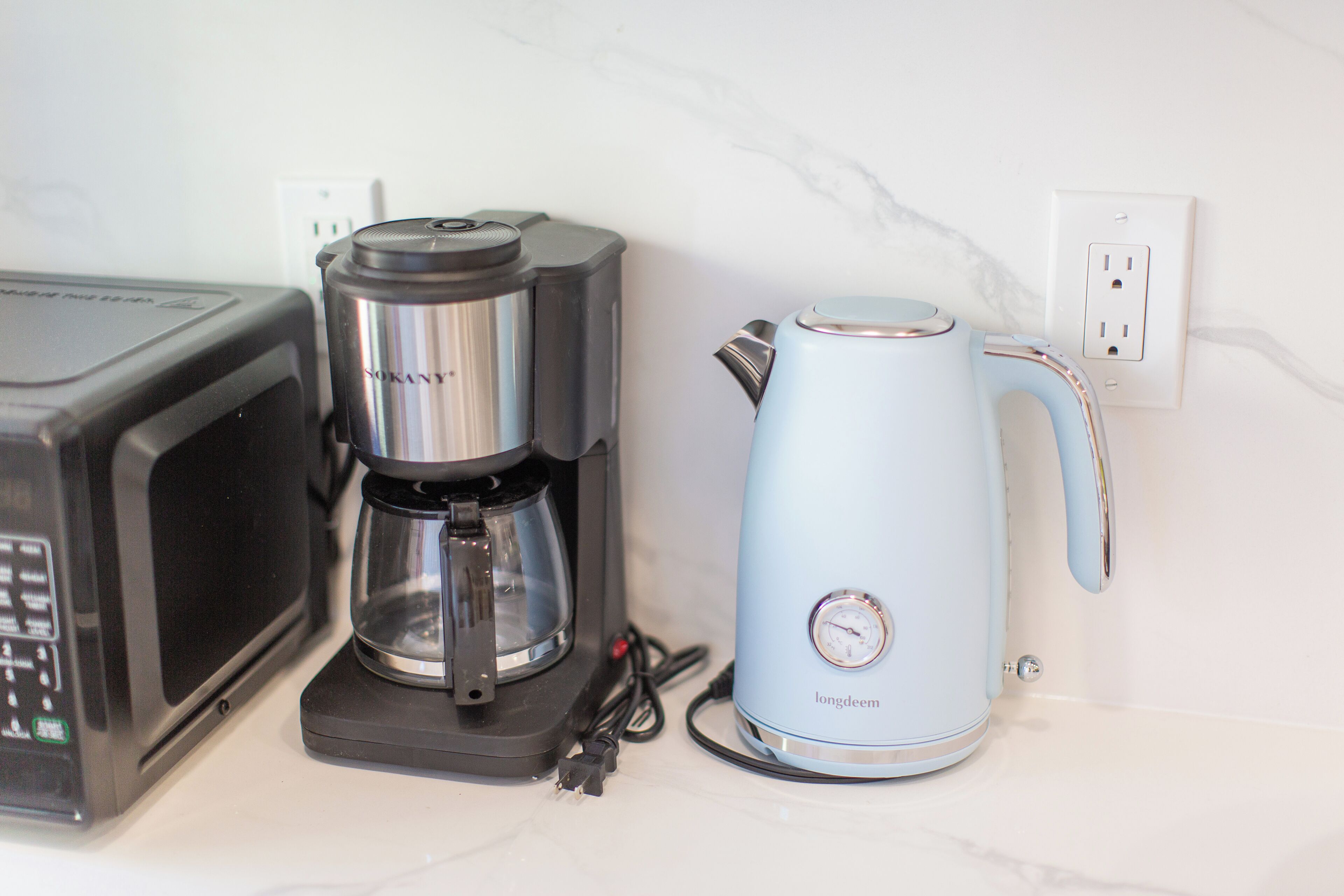 Un four à micro-ondes, une machine à café et une bouilloire sont posés sur un plan de travail.