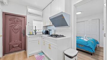 A compact kitchen with white cabinets, a stove, and a microwave. There's a patterned rug on the floor and a door with intricate design.