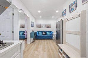 Une cuisine moderne avec un plan de travail blanc, un canapé bleu et un coin repas comprenant une table et des chaises blanches.