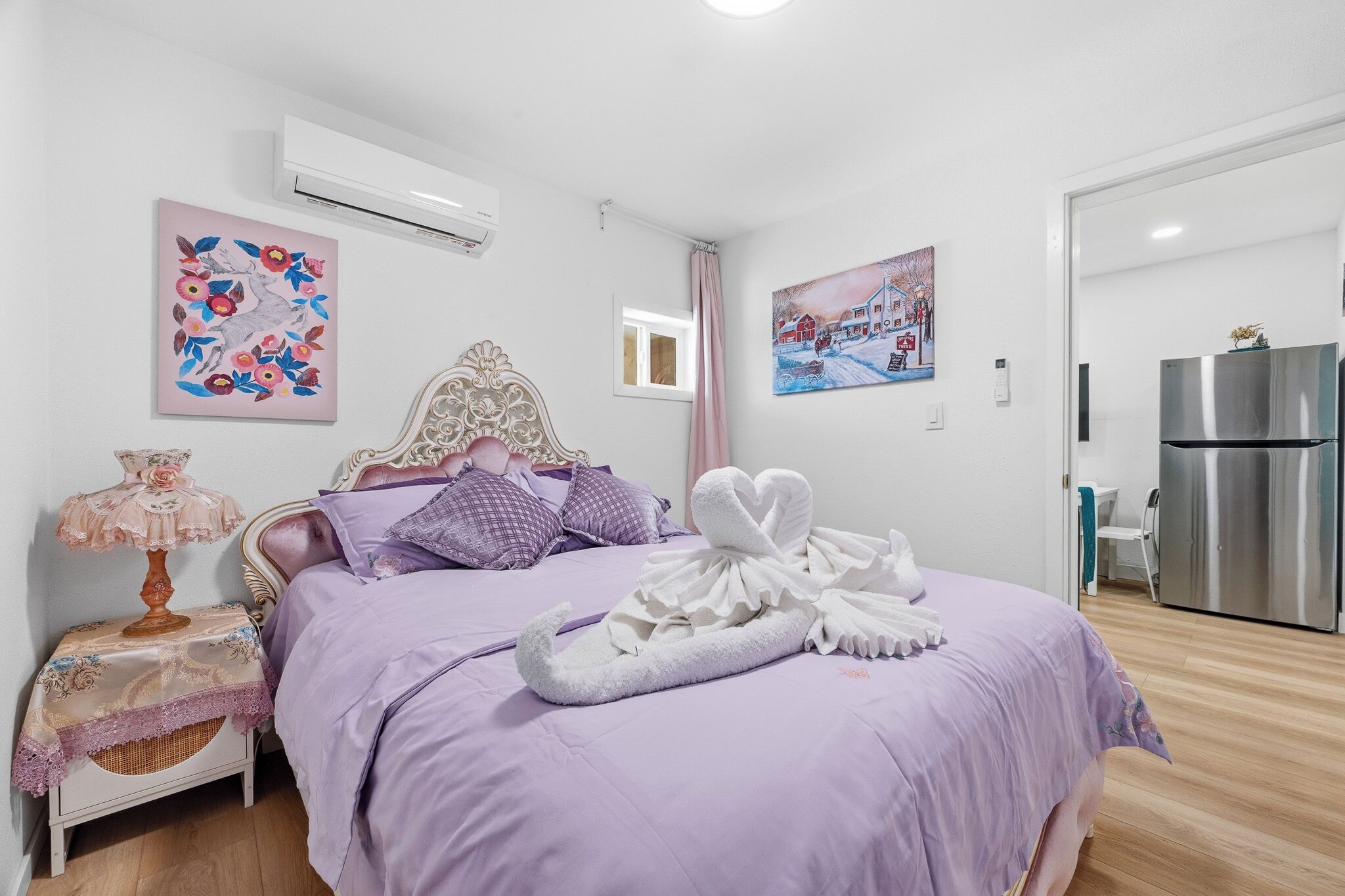 Una camera da letto con un letto, un comodino con una lampada, un condizionatore d'aria a parete e un frigorifero nella stanza adiacente.