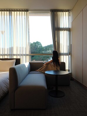A hotel room with a large window, a sofa, a small round table, and a bed. - Hotel TOV (Busan)