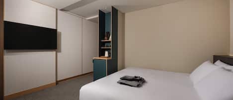 Habitación de hotel con cama, televisor montado en la pared y pequeña zona de kitchenette.