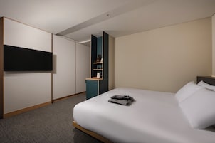 A hotel room with a bed, a TV mounted on the wall, and a small kitchenette area.