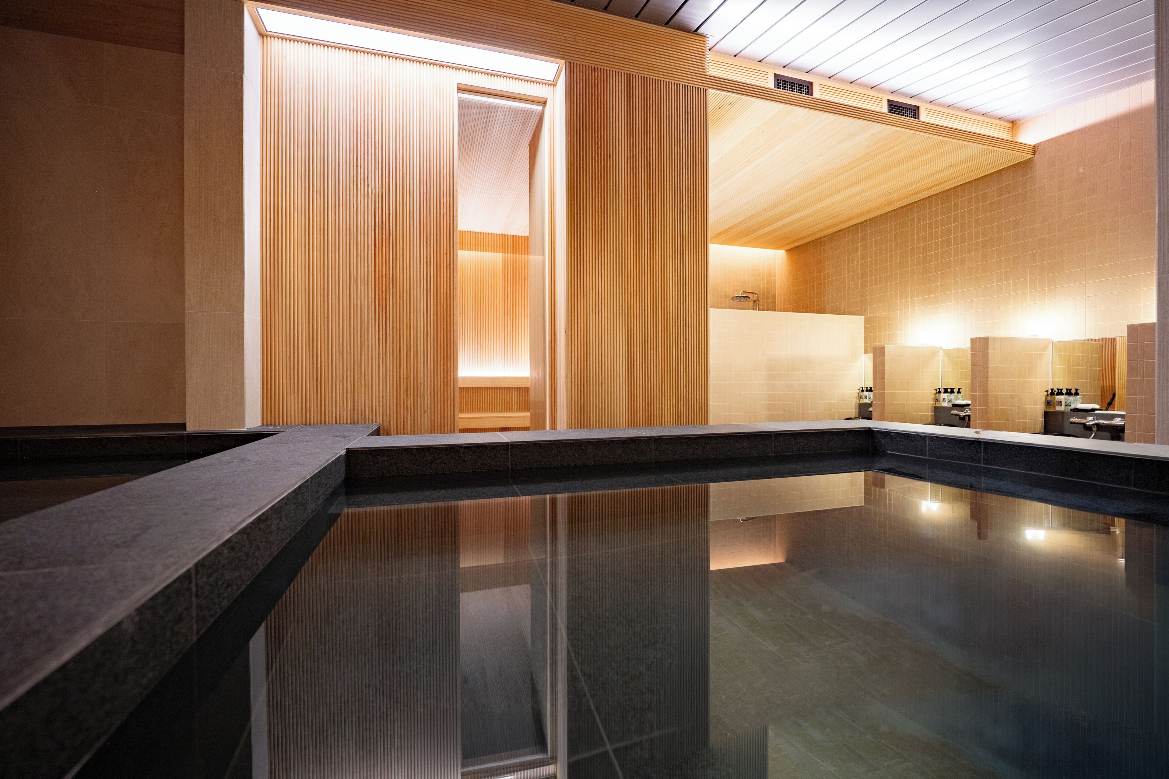 A modern indoor pool area with a clear water surface, wooden panel walls, and a ceiling with a slatted design.