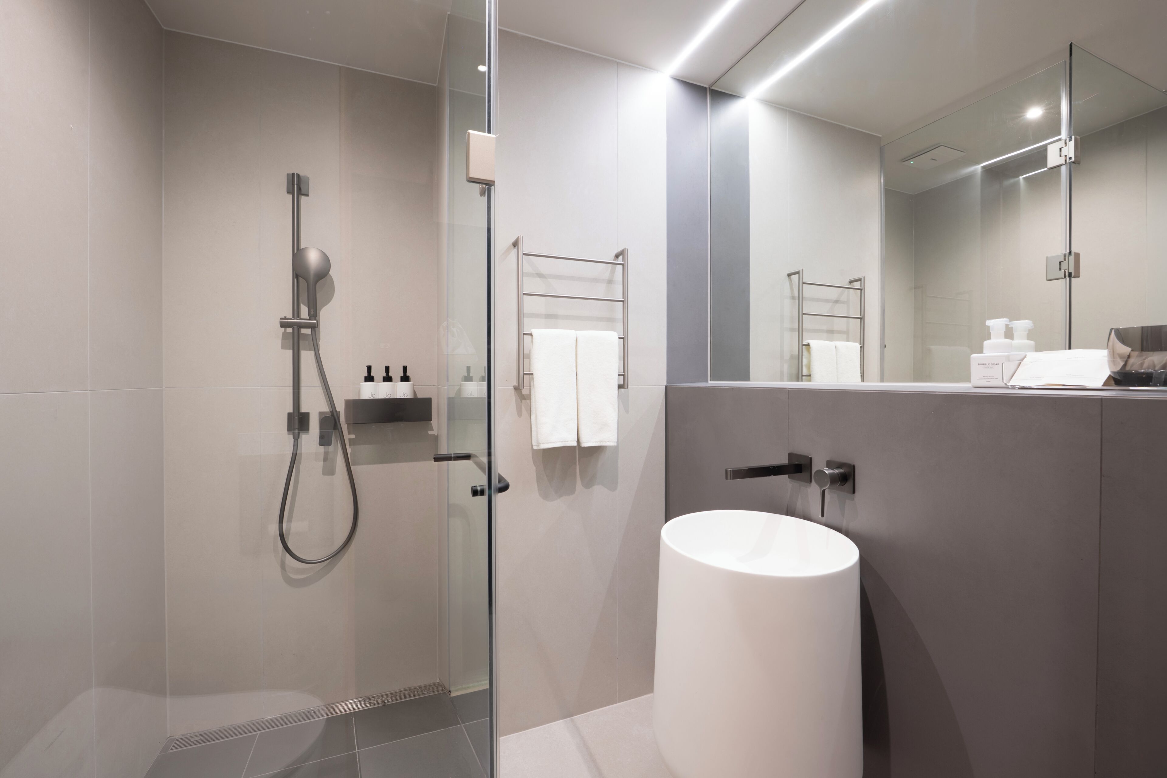 Un baño moderno con ducha envuelta en vidrio, lavamanos blanco y un espejo grande.