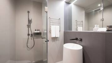 Un baño moderno con ducha envuelta en vidrio, lavamanos blanco y un espejo grande.