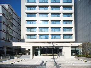 Un moderno edificio de hotel con entrada despejada, varios pisos y un establecimiento visible de café y panadería.