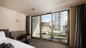 Een hotelkamer met een bed, een bank, een klein tafeltje en een balkon met uitzicht op de stad.