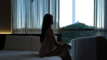 A hotel room with a bed, a chair, and a view of a tower through sheer curtains.