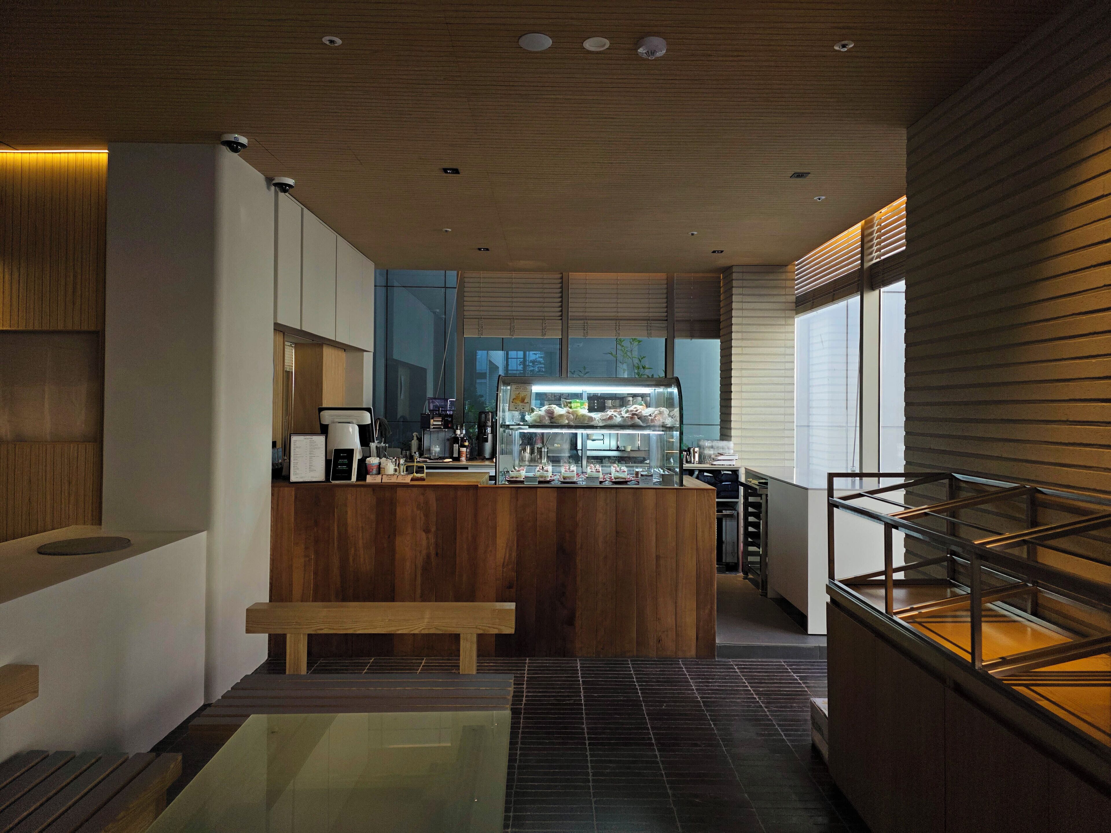 A modern kitchen with a wooden counter, a coffee machine, and a display case with food items.