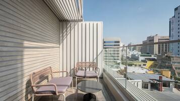 A balcony with two wicker chairs and a small table, overlooking a cityscape with modern buildings.