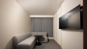 Een moderne hotelkamer met een modulaire bank, een klein rond tafeltje en een flatscreen televisie aan de muur.