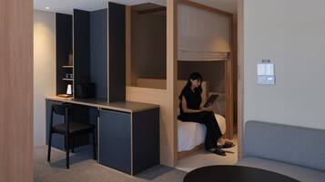 A compact hotel room with a desk, chair, bed, and a sofa.