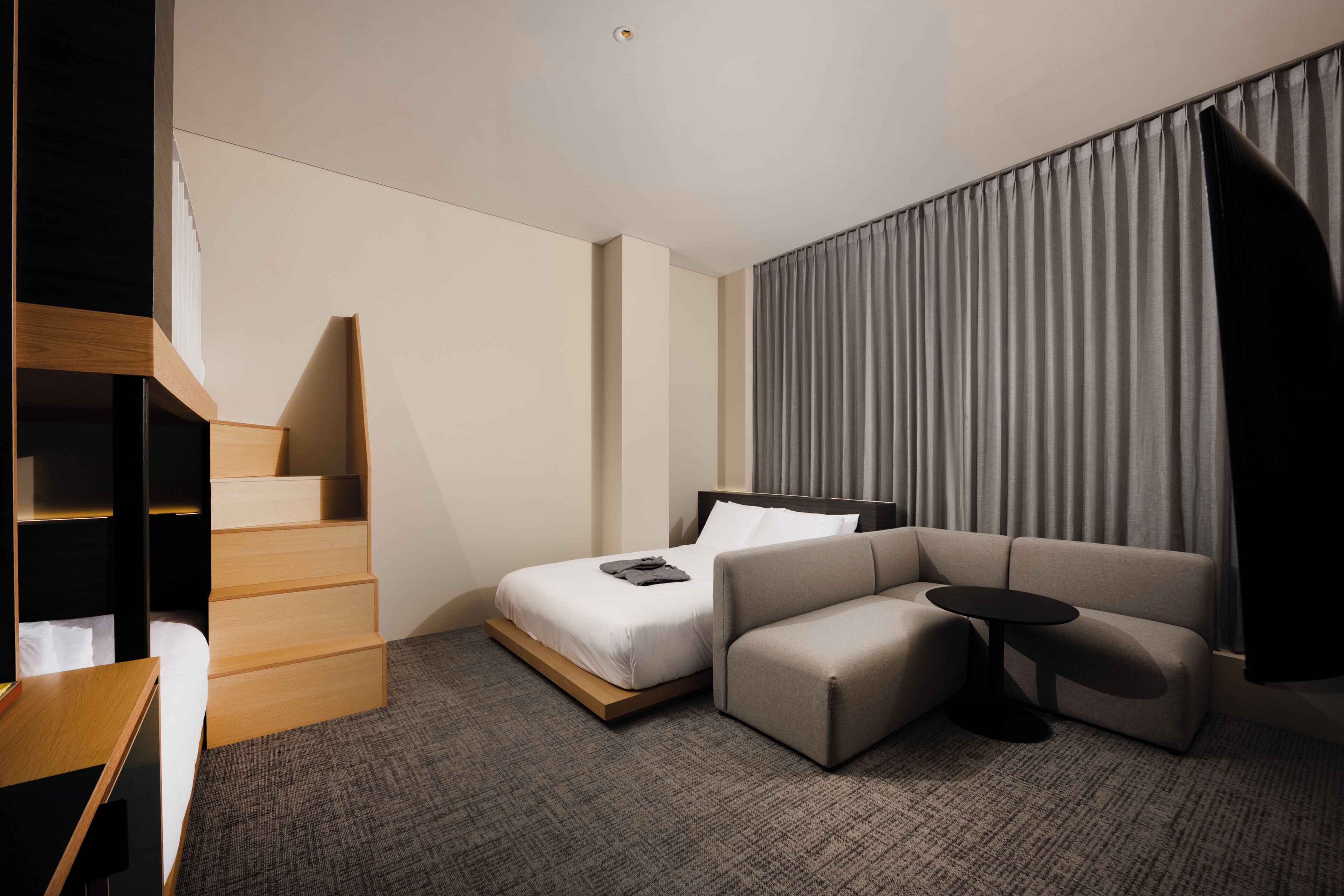 Quarto de hotel moderno com cama, sofá, mesa pequena e escada.