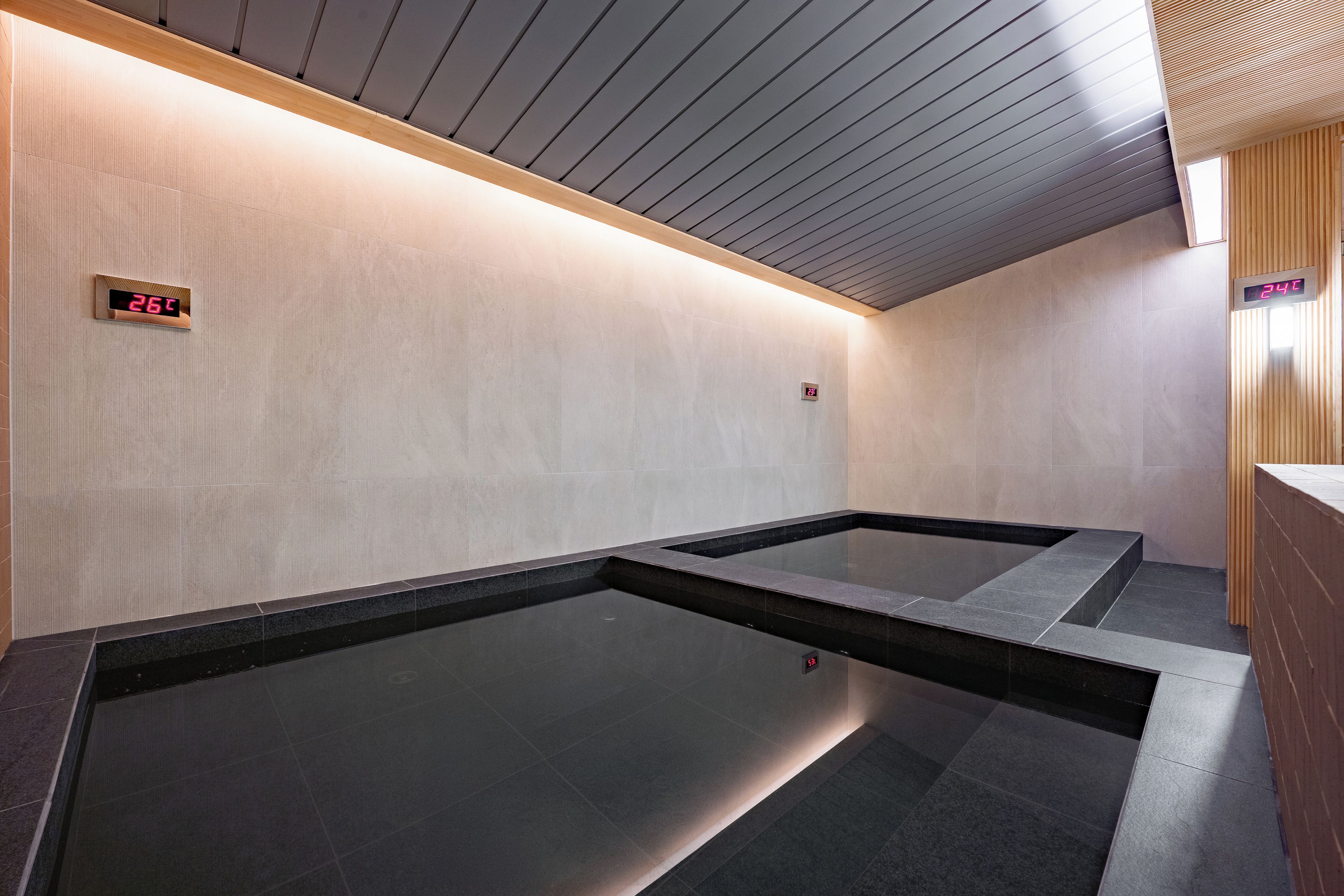 Un baño moderno con un piso oscuro y grande, techo de madera y un panel digital que muestra la temperatura.