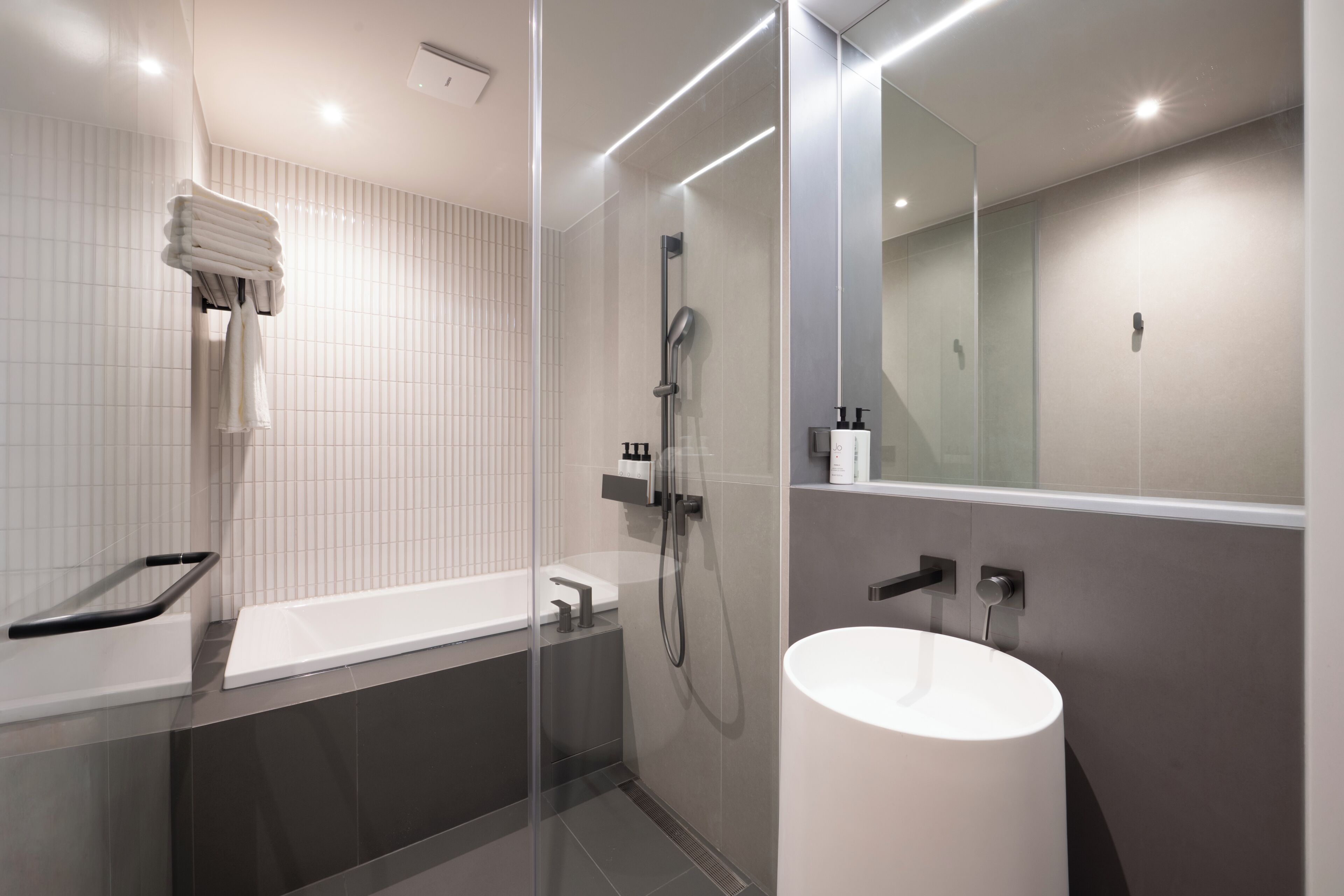 A modern bathroom with a glass-enclosed shower, a white bathtub, and a large mirror.
