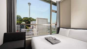 A hotel room with a large window, a bed, a chair, and a view of a tower.