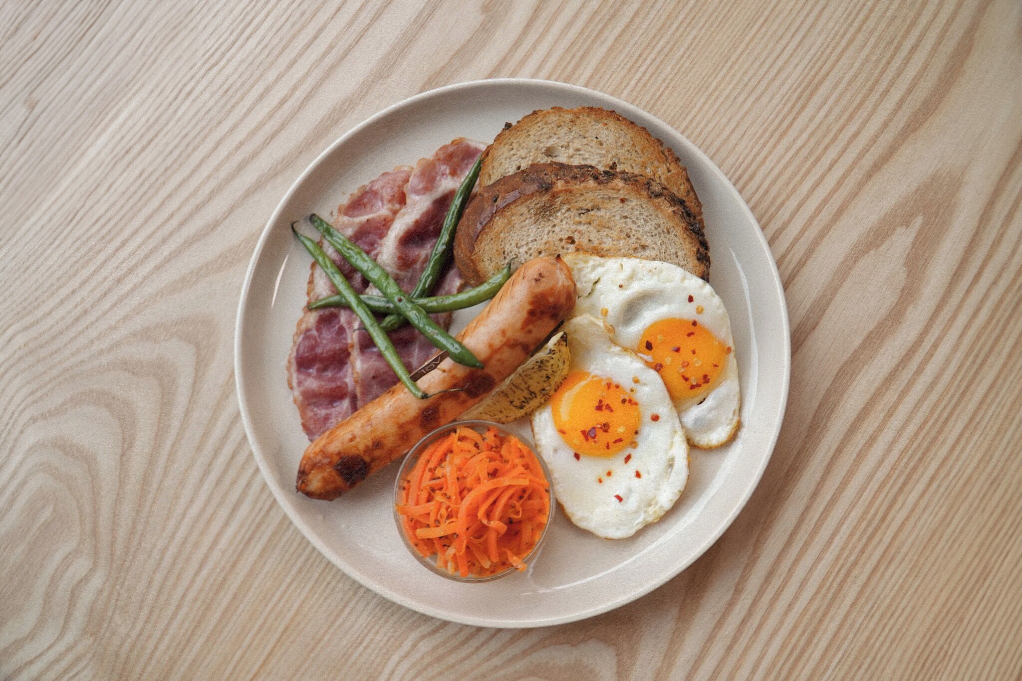 A plate with eggs, sausage, bacon, toast, and a side of carrot salad.