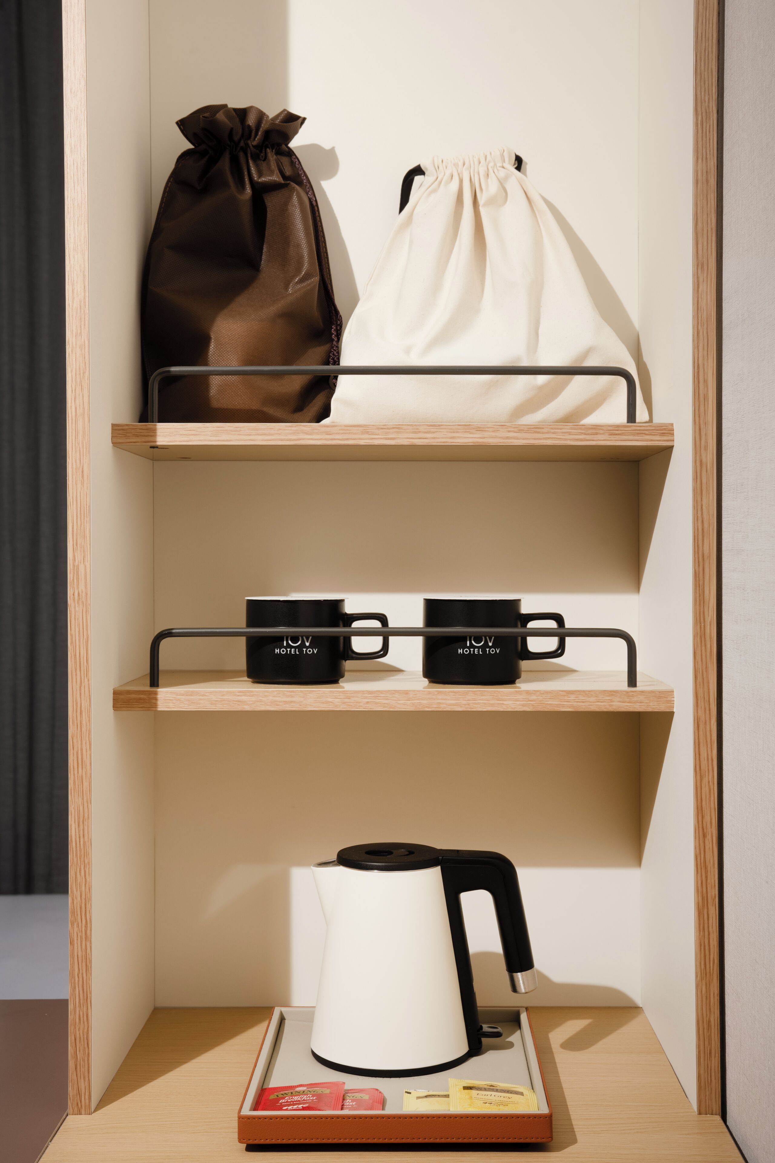 Une étagère avec un sac marron, un sac blanc à cordon de serrage, deux tasses noires et une bouilloire blanche.
