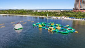 Un parque acuático con estructuras inflables, una torre de salvavidas y una zona de playa con sombrillas.
