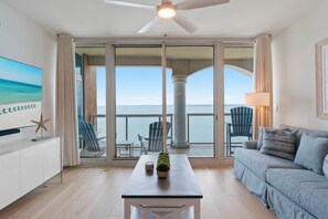 A modern living room with a balcony, a ceiling fan, a flat-screen TV, and a view of the sea. - Portofino Blissful Gulf and Sound Views (Escambia County)