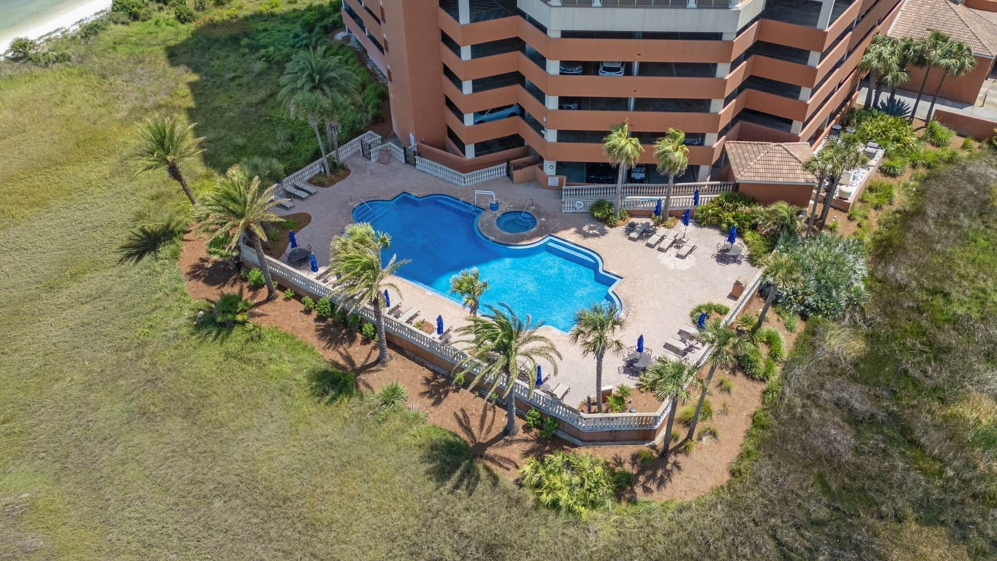 An aerial view of a hotel with a swimming pool surrounded by palm trees and lounge chairs.