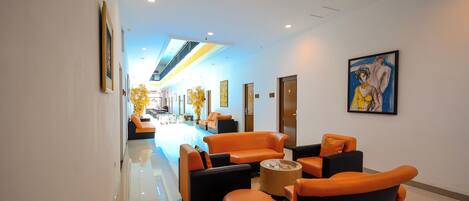 A hotel lobby with a checkered floor, orange and black seating, a central coffee table, and a painting on the wall.