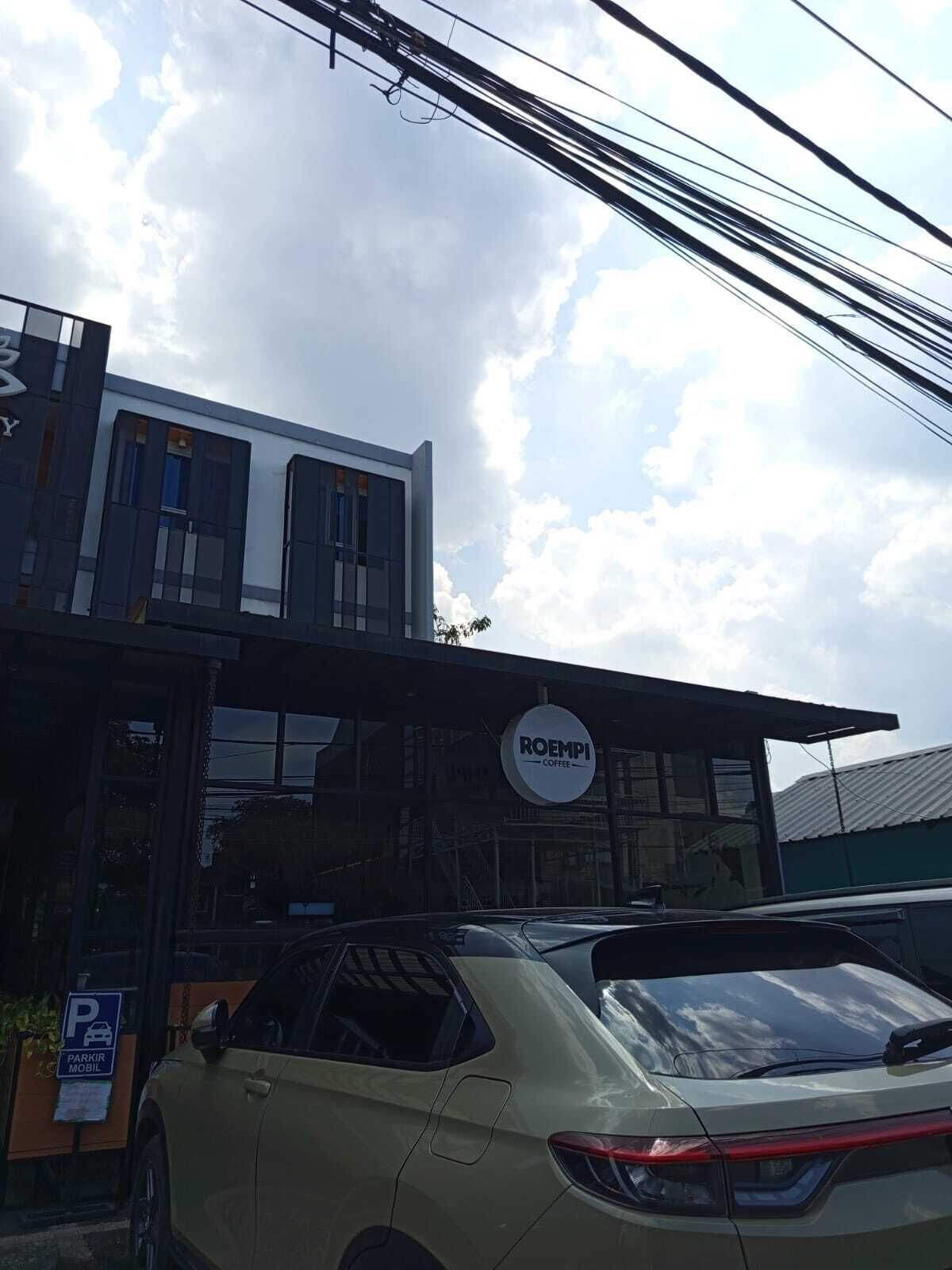 A building with a sign for 'ROEMPI Coffee' and a parking sign indicating 'PARKIR MOBIL'.