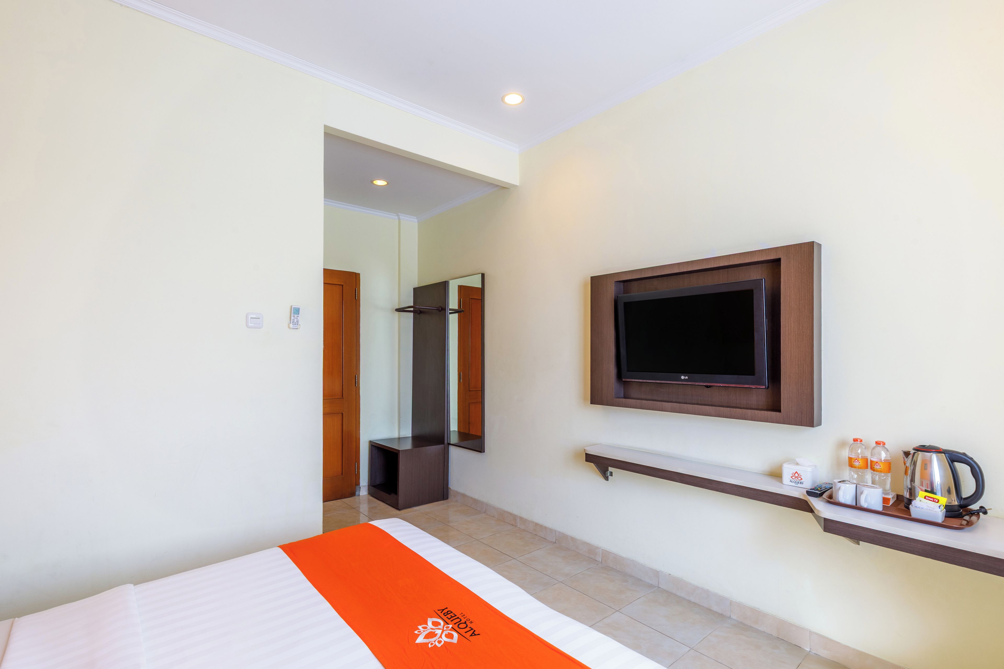 Ein Hotelzimmer mit Bett, einem an der Wand befestigten Fernseher, einer kleinen Ablage mit Pflegeprodukten und einem durchgehenden Türspalt einsehbaren Badezimmer.