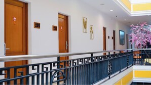 Un pasillo de hotel con puertas de madera, placas con los números de las habitaciones y barandilla de balcón.