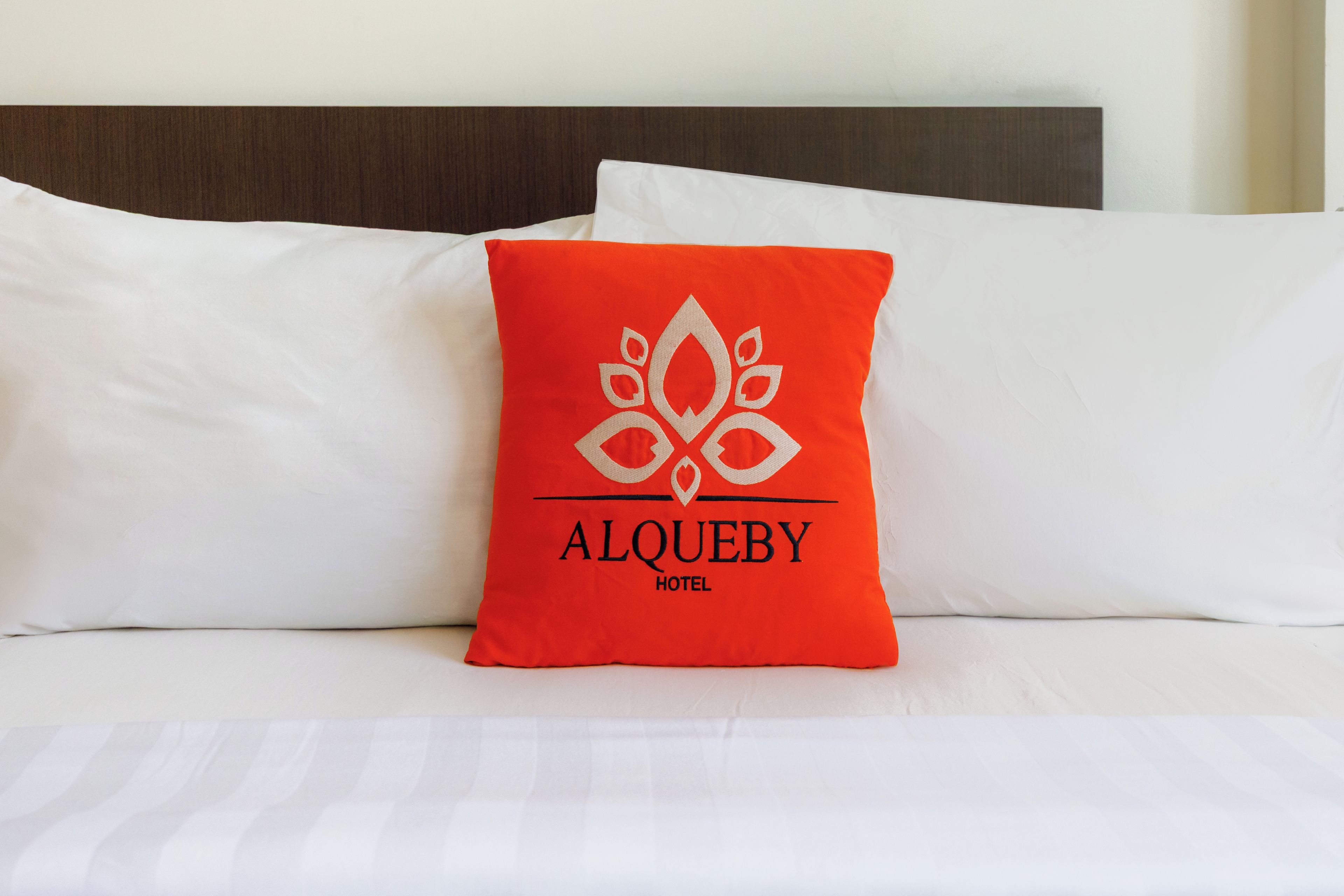 A bed with white bedding and a red pillow with a logo and text.