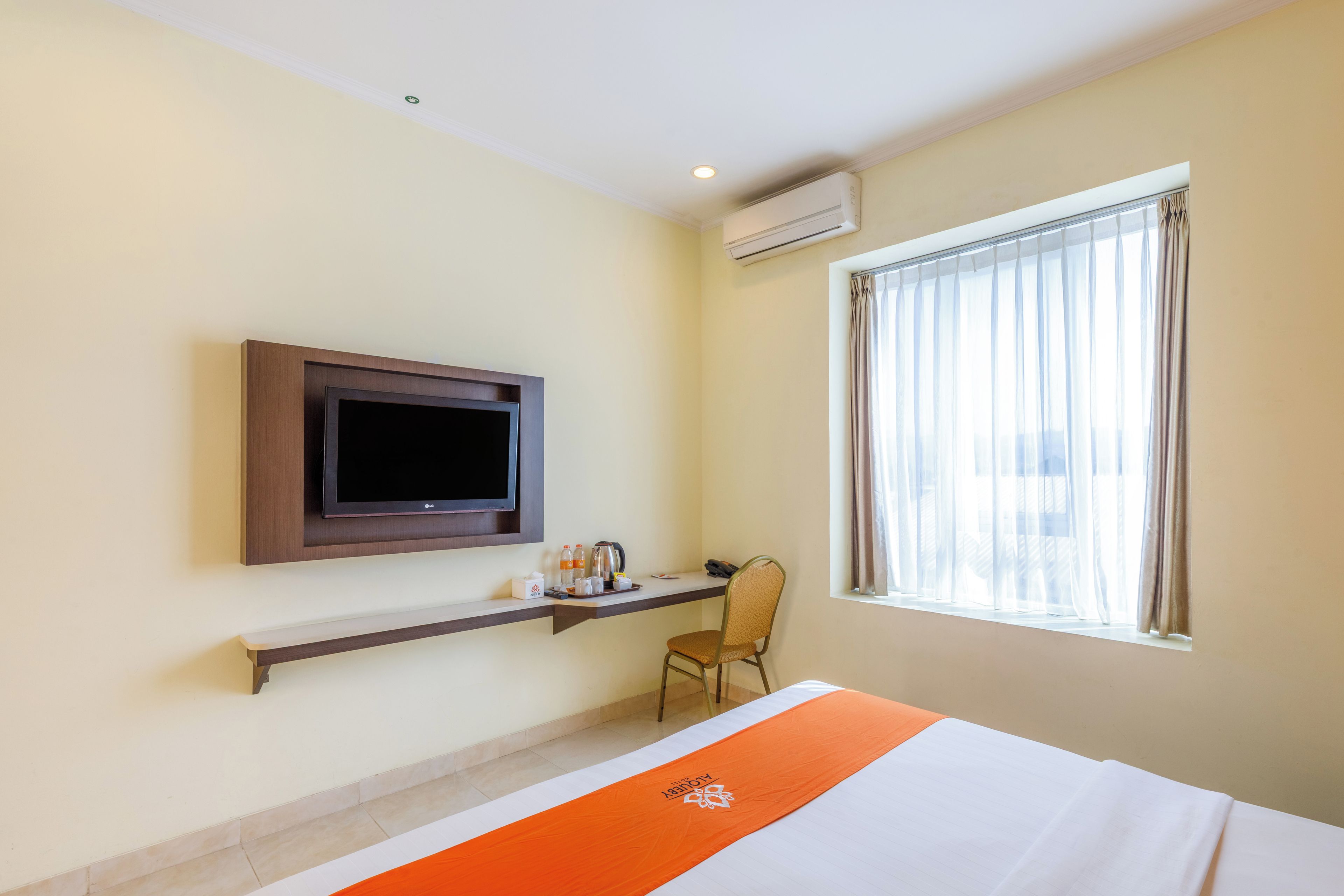 Una habitación de hotel con cama, televisor montado en la pared, escritorio con silla y ventana con cortinas.