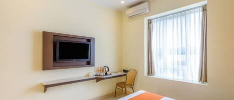Una habitación de hotel con cama, televisor montado en la pared, escritorio con silla y ventana con cortinas.