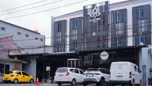 Un hotel con fachada moderna, un cartel que dice 'ALOQUEBY HOTEL' y un cartel de 'ROEMPI COFFEE'. Hay coches aparcados en la calle.