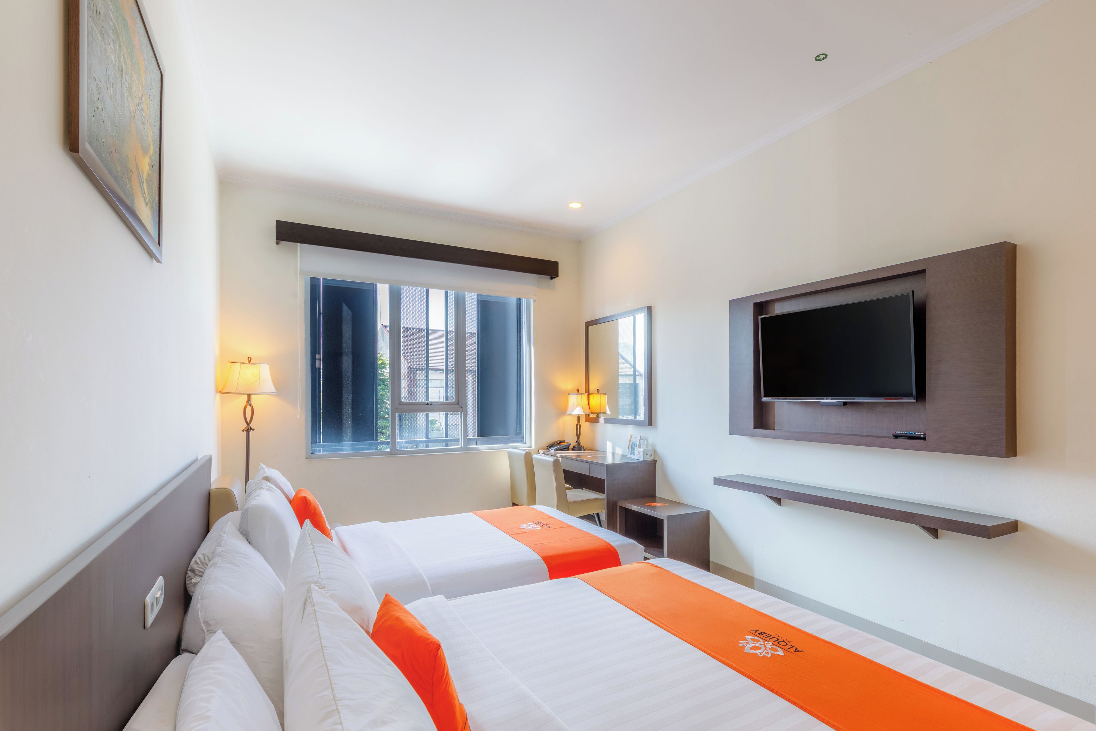 A hotel room with two beds, a desk, a TV, and a window with curtains.