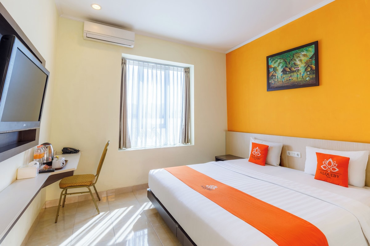 A hotel room with a bed, a television, a window with curtains, a painting on the wall, and a chair.