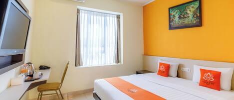 A hotel room with a bed, a television, a window with curtains, a painting on the wall, and a chair.