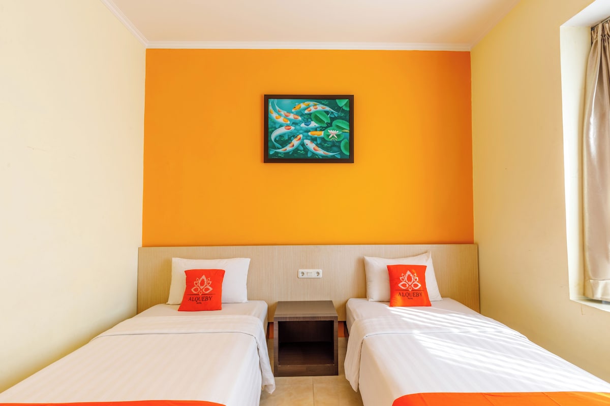 A hotel room with two single beds, a nightstand, a painting on the wall, and a window with curtains.