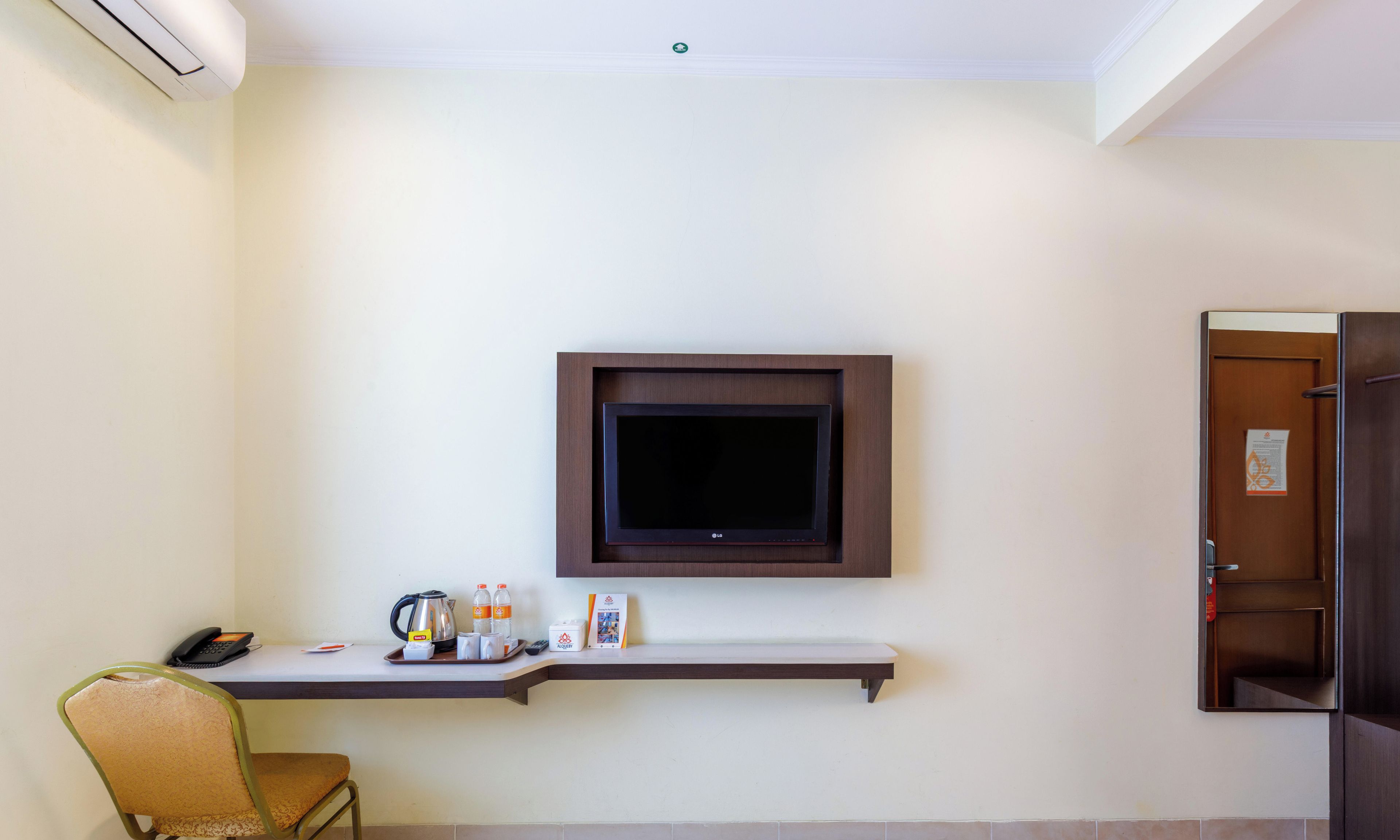 Habitación de hotel con televisor de pantalla plana en la pared, una mesita con un teléfono, una tetera y algunos artículos de aseo.