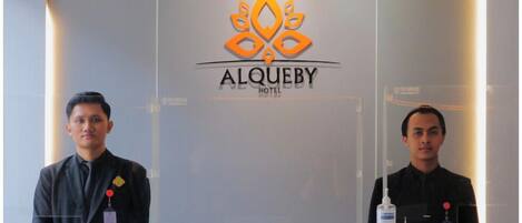 A reception desk at Alquevy Hotel with a modern design, featuring a logo and a sign indicating cashless payment options.