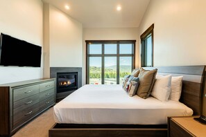 Ein Schlafzimmer mit Bett, Fernseher, Kamin und großem Fenster.