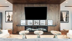 Ein modernes Wohnzimmer mit großem Flachbildfernseher, einer Holzwandverkleidung, gerahmten Kunstwerken und Couchtischen mit Marmorplatten.
